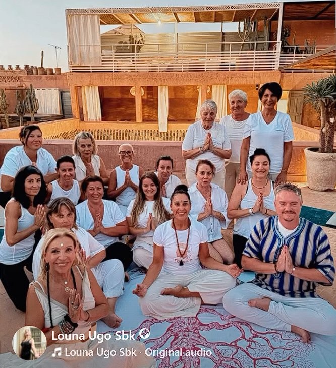 Groupe en retraite yoga sur le rooftop panoramique 60m² à Marrakech — posture namaste au coucher du soleil